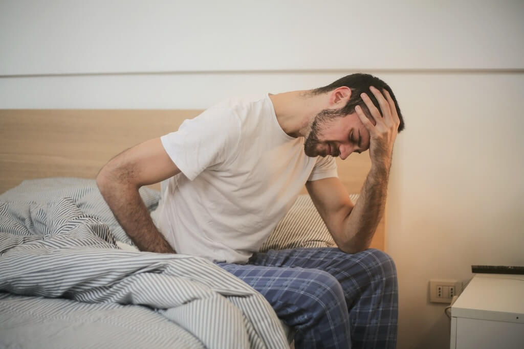 man sitting on edge of bed holding his head