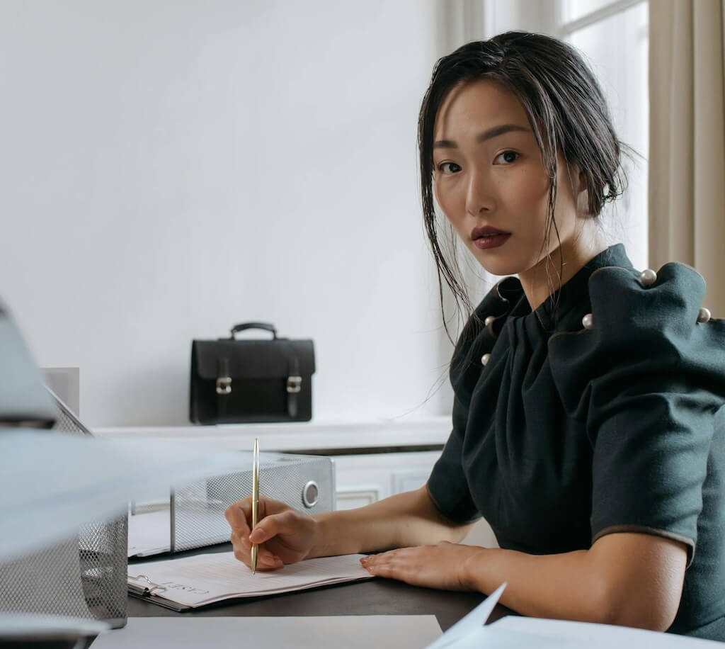 woman sitting at desk with pen in front of various documents