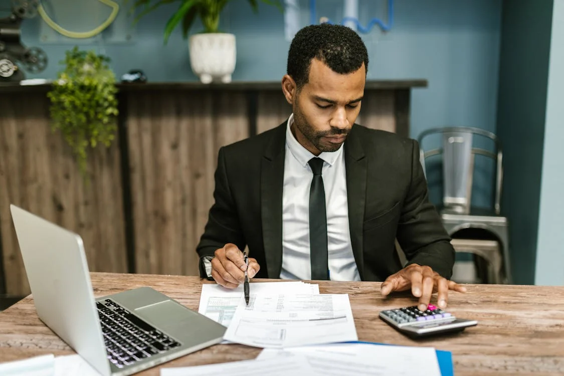 man in black suit doing calculations and working on laptop