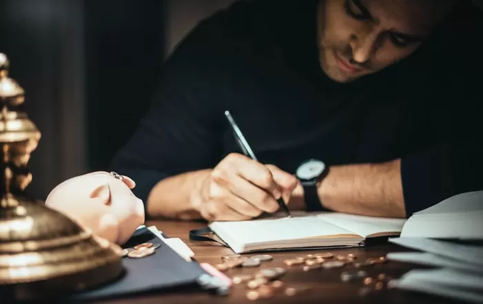 man writing in notebook with pieces of change in front of him