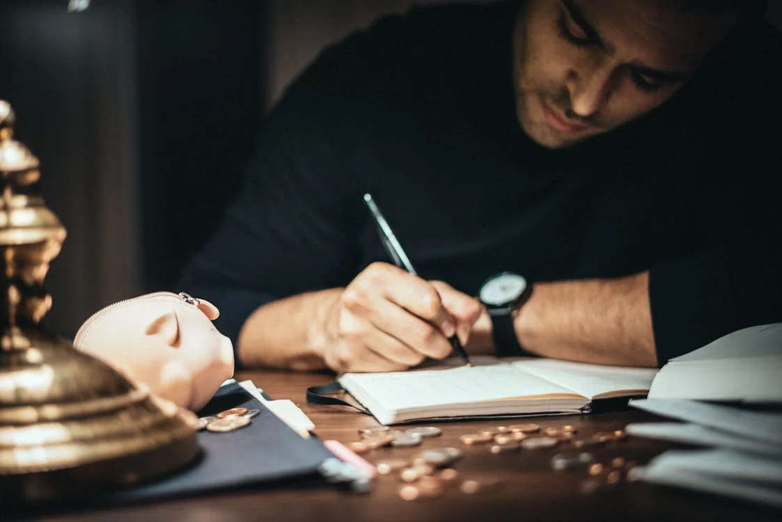 man writing in notebook with pieces of change in front of him