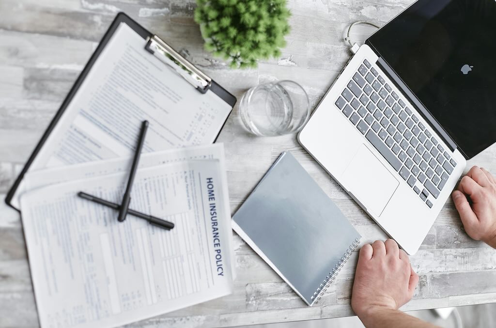 home insurance policy paperwork next to laptop and notebook on desk