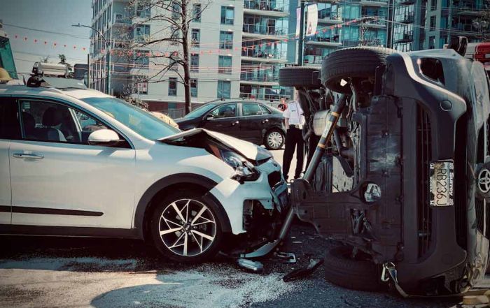 A picture of a white car crashed into another car that is flipped onto its side