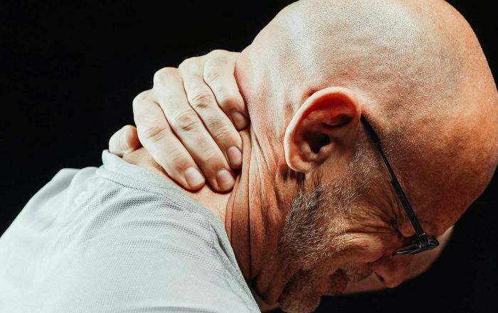 A man grimacing, holding the back of his neck