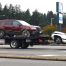 A tow truck driving with two damaged vehicles attached to it