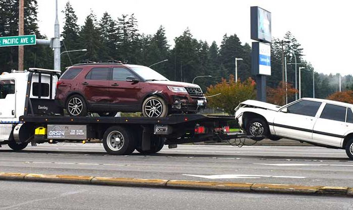 A tow truck driving with two damaged vehicles attached to it