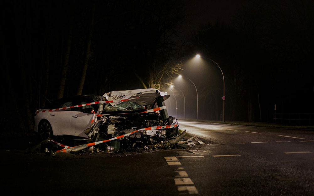 A wrecked vehicle, taped off, alone on the side of street light lit road
