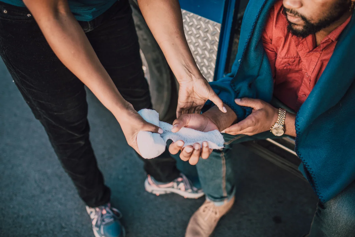 A person in a truck having their wrist wrapped by another person